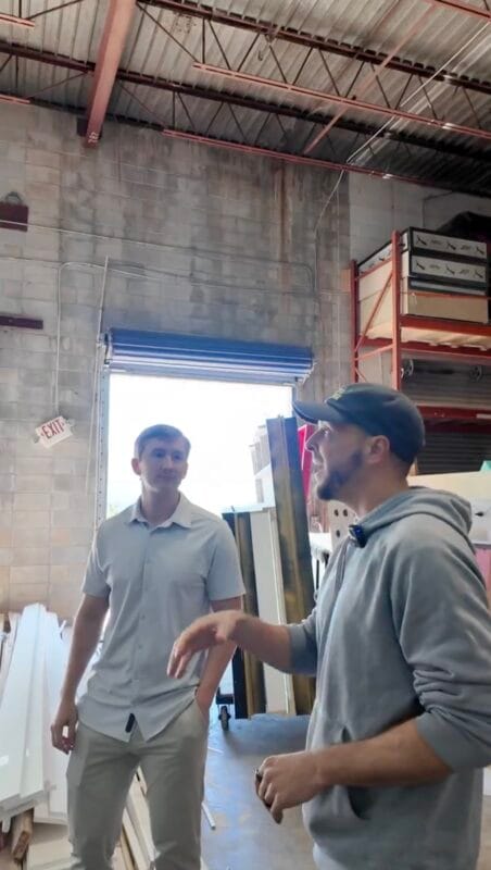 Two men talking inside an event decor warehouse near a loading dock door, surrounded by large white panels and shelving