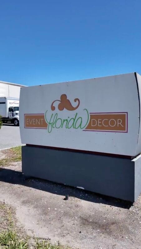 Outdoor monument sign for Event Florida Decor against a bright blue sky, with a truck and commercial buildings in the background