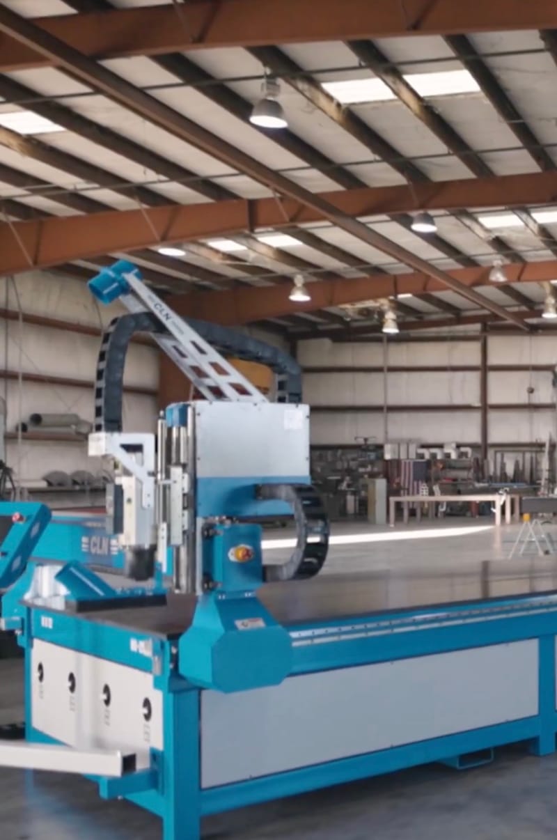 CLN-branded blue CNC router on the factory floor of a large open warehouse, ceiling lights and steel structure visible overhead